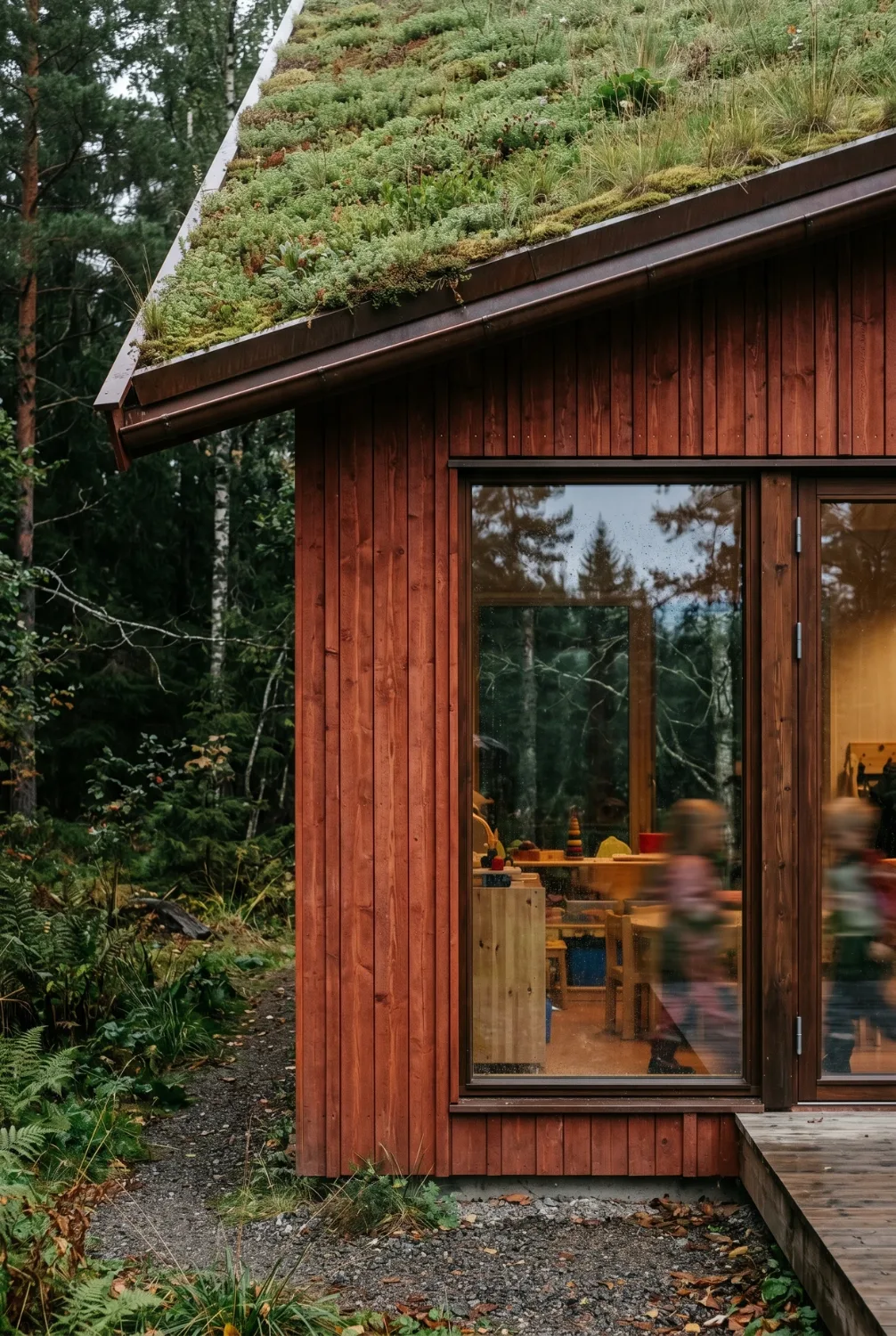 Architectural visualisation — close detail of the red timber facade meeting the green sedum roof, a window onto the playroom